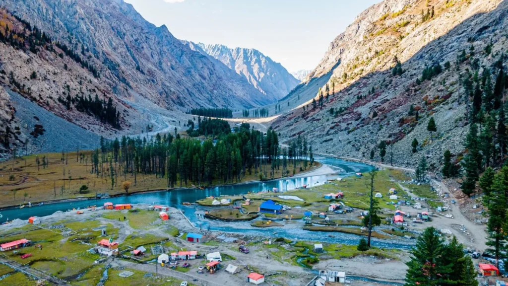 A stunning aerial view of Swat Valley, featuring scattered colorful houses nestled in a green valley surrounded by dramatic rocky mountains, pine forests, and winding streams.