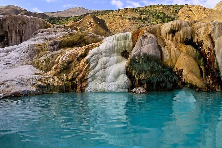 Natural hot spring pool with turquoise water surrounded by mineral-rich rocky formations and dry mountain terrain at Garam Chashma in Chitral Valley, Pakistan.