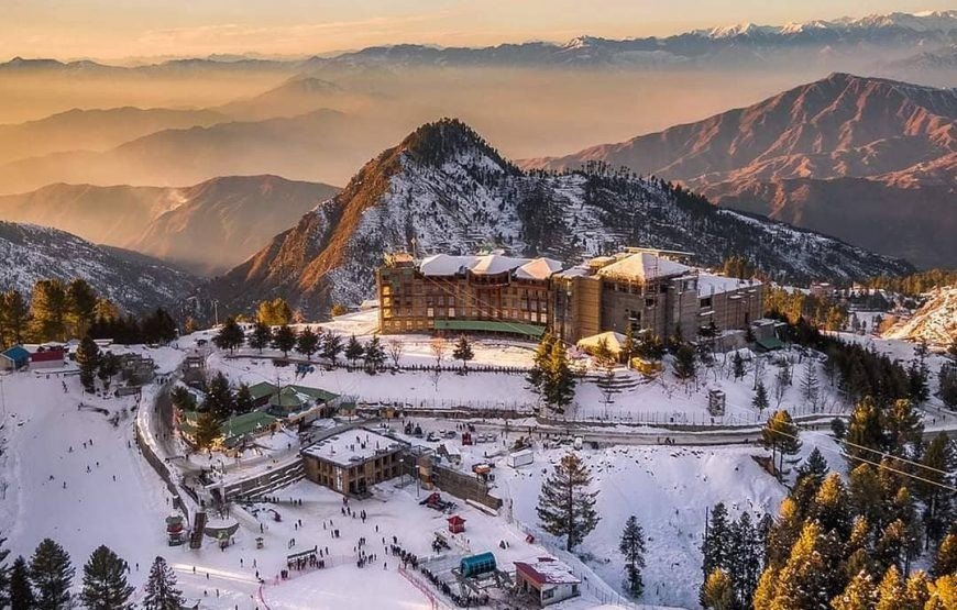 A breathtaking winter landscape of Malam Jabba with snow-covered pine trees, mountain ridges glowing under a golden sunset, and scattered visitors enjoying the serene highland terrain.