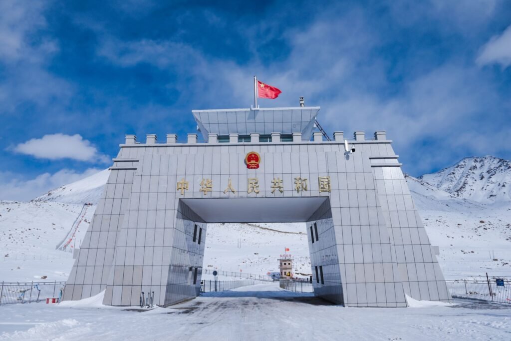 The grand white gateway at Khunjerab Pass covered in snow, marking the Pakistan-China border amid rugged mountains and a bright blue sky.