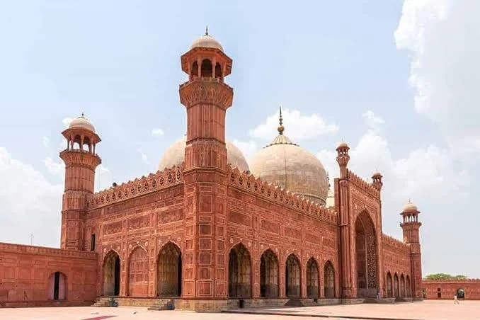 Wide-angle view of the Badshahi Mosque in Lahore showcasing its grand red sandstone exterior, large domes, and tall minarets under a bright sky