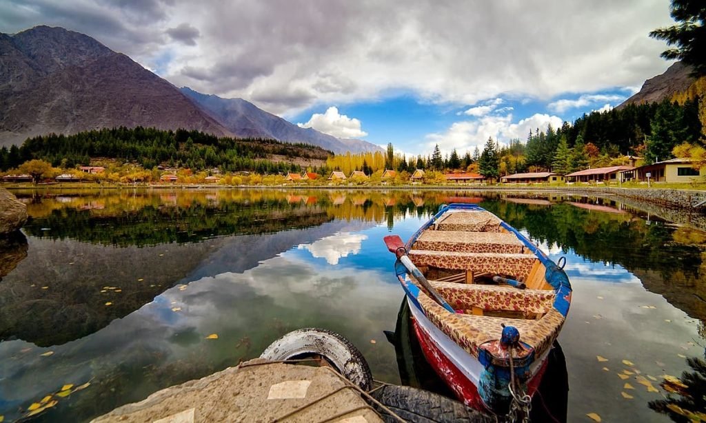 A serene lake in Pakistan reflecting cloudy skies and mountain peaks, with a colorful traditional boat docked in the foreground, symbolizing the country's natural beauty and tourism potential.
Pakistan Tourism Aug 202