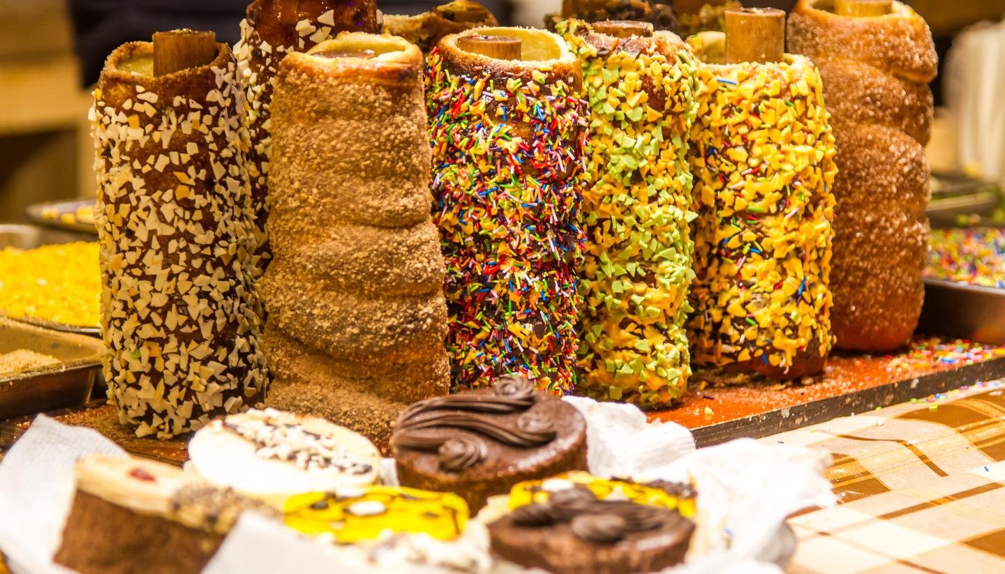 Colorful assortment of Trdelník, a popular Czech street pastry, topped with nuts, chocolate, and sprinkles, displayed at a market stall in Prague.