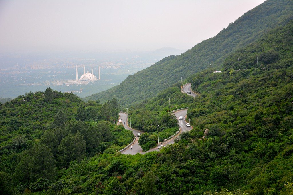 Panoramic view of winding road through lush green Margalla Hills with Faisal Mosque visible in the background, representing Islamabad’s iconic hiking destination.